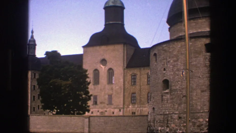 1975 Copenhagen 8mm frame with a domed roofline, stone tower, arched windows, tree, wall, and mast-like pole near the water.