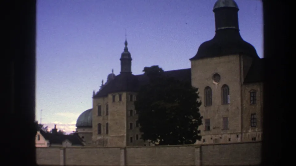 A 1975 Copenhagen frame shows historic tan buildings, a green dome, dark roofs, and a tree viewed from a shadowed opening.