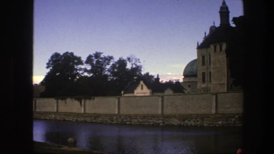 1975 Copenhagen frame with river in the foreground, a long wall, silhouetted trees, and the edge of a historic towered building.