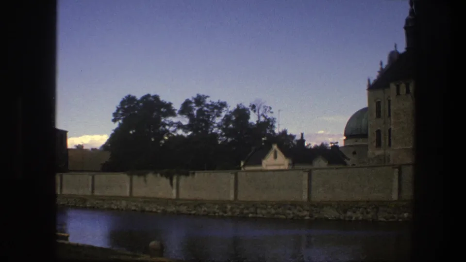 1975 Copenhagen home-movie frame showing the river foreground, perimeter wall, trees, and partial historic building with dome.