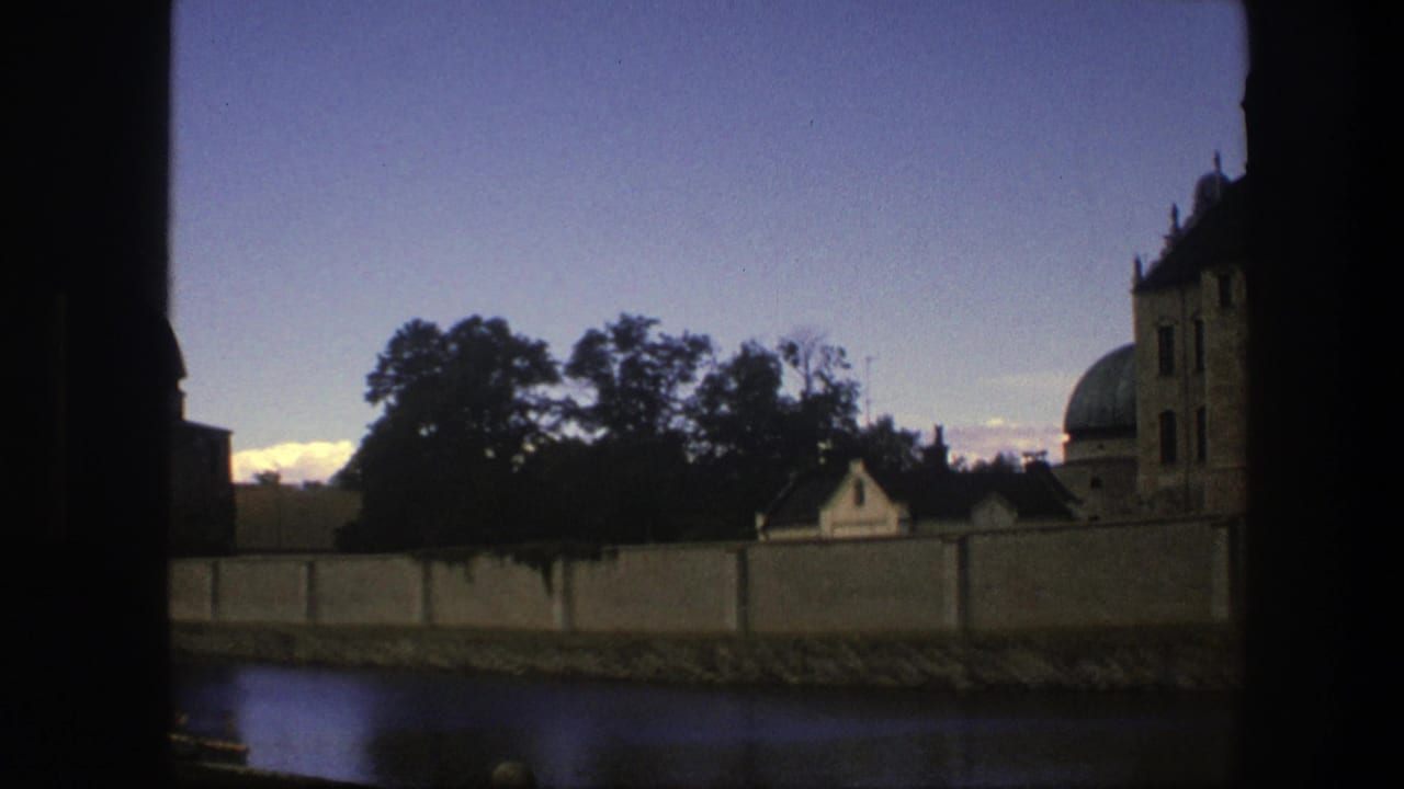 1975 Copenhagen home-movie frame showing a domed stone structure, wall, trees, and water under a blue evening sky.