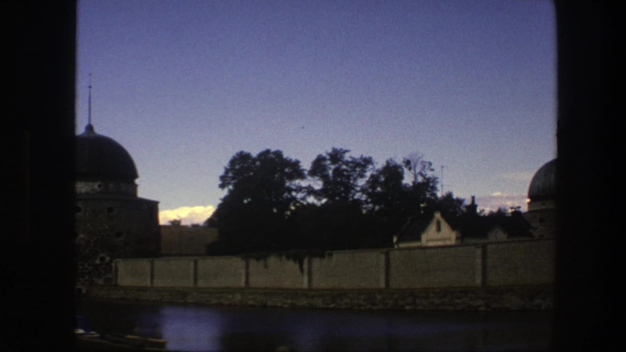 Waterfront wall, trees, rooftops, and part of a domed tower at dusk.