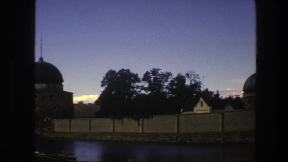 1975 Copenhagen frame with a domed tower partly visible beyond trees and a long wall along the water.