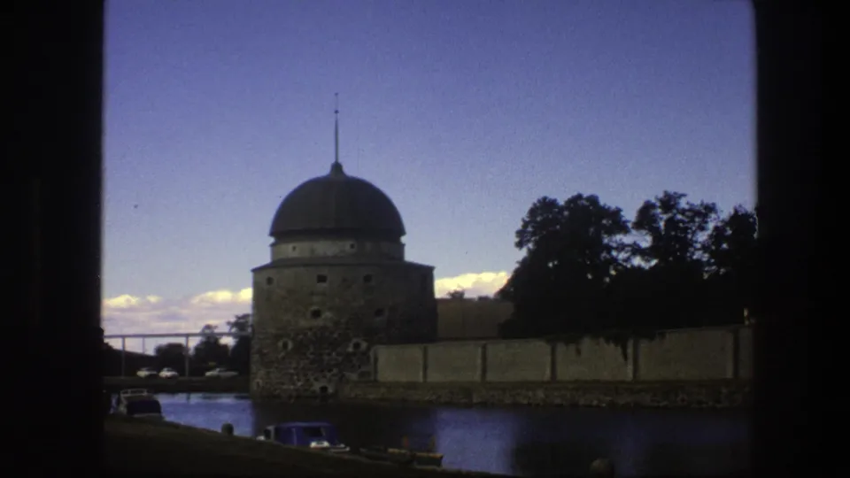 1975 Copenhagen frame showing the domed tower, waterside wall, trees, and parked cars in low evening light.