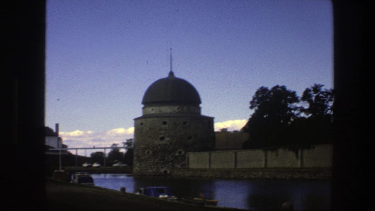 1975 Copenhagen home-movie frame showing a domed waterside structure, parked cars, trees, and dark film-frame edges.