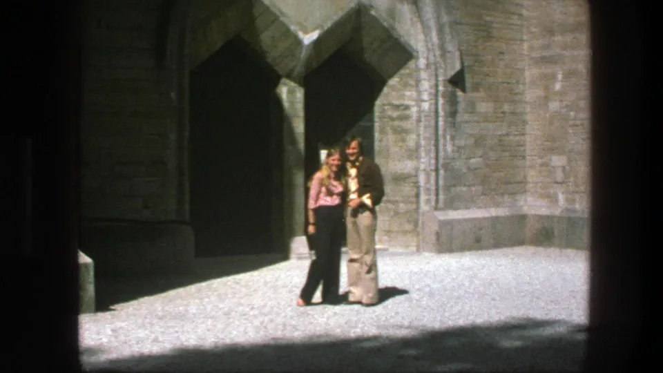The couple appears to embrace or kiss outside the Copenhagen stone church entrance, surrounded by sunlit masonry and shadow.