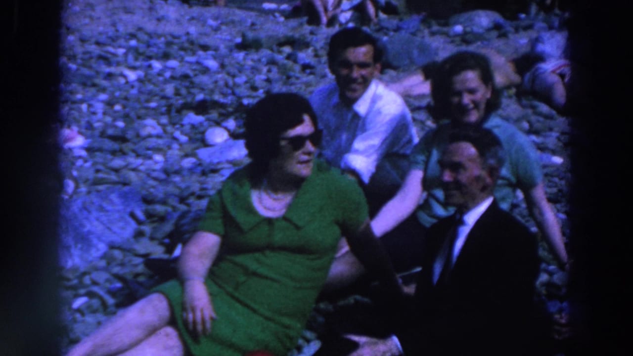 Five adults sit on gray rocks, with a woman in a green dress and sunglasses in front.