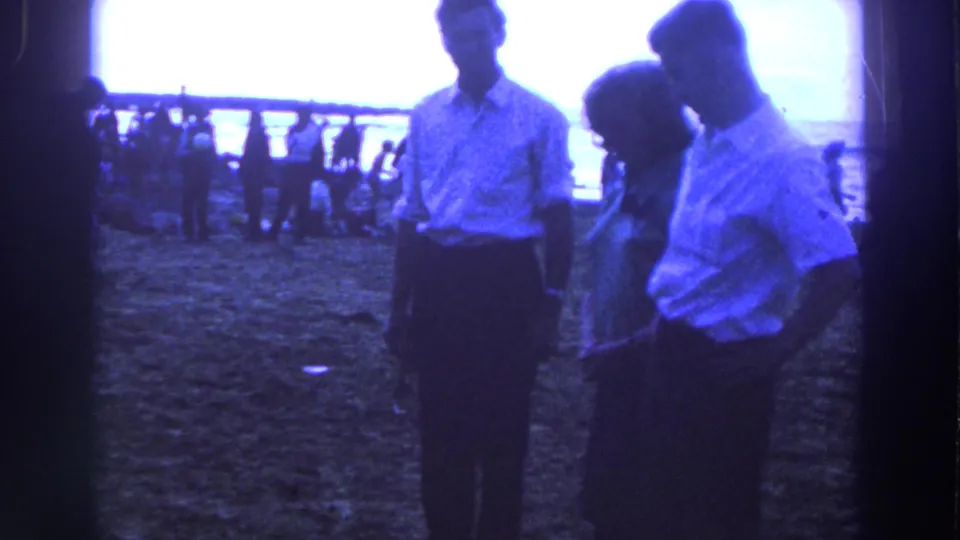 The adults remain grouped in the Irish outdoor scene, with the woman between two men and a crowd beyond the railing.