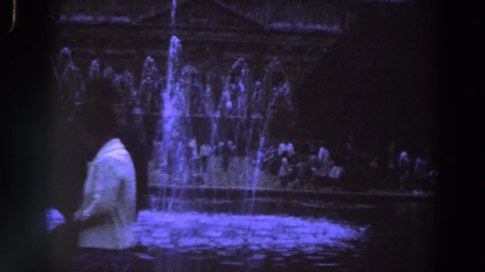 1961 Ireland frame showing a man in front of blue-lit fountain jets and background visitors at night.