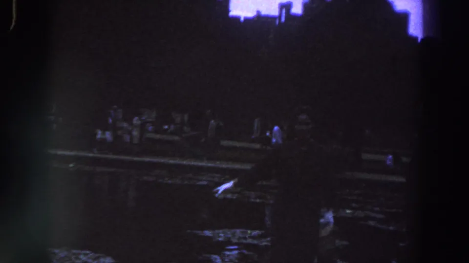 1961 Ireland footage shows people gathered along a dark waterside edge, with a bright pale reflection on rippling water.