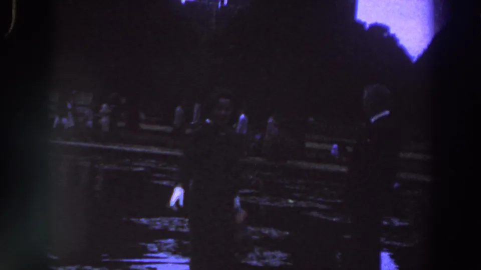 1961 Ireland home-movie frame with two foreground silhouettes and additional adults near a dark, reflective waterfront.