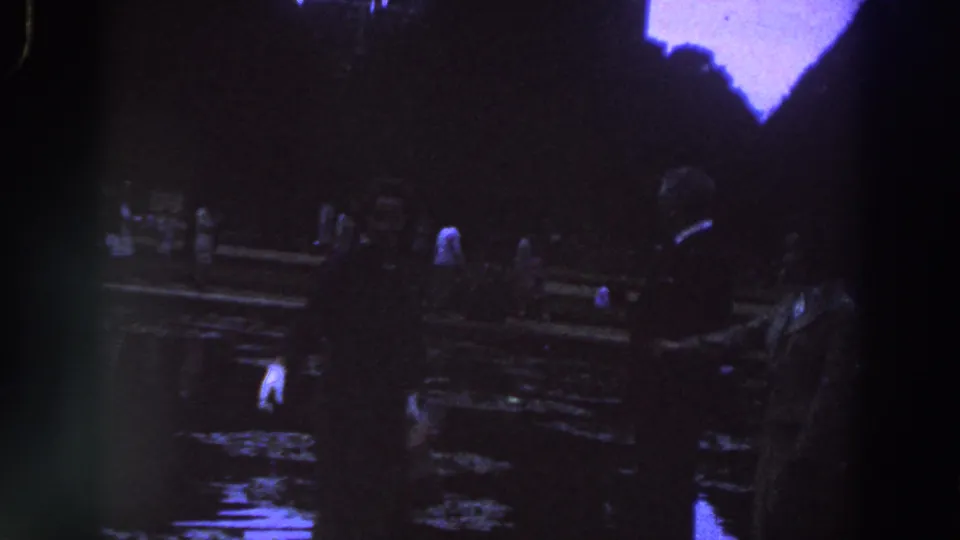 1961 Ireland frame showing shadowed adults beside reflective water, with indistinct formal clothing and deep nighttime exposure.