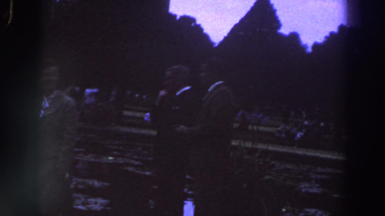 1961 Ireland 8mm frame showing dimly lit people near a statue or monument base in a public plaza.