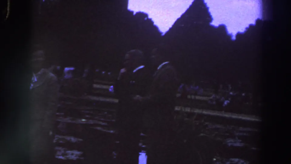 1961 Ireland 8mm frame showing dimly lit people near a statue or monument base in a public plaza.