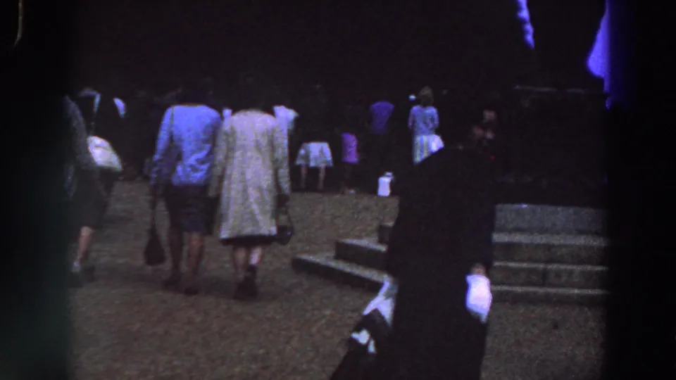 1961 Ireland 8mm frame showing adults in coats walking through a plaza toward steps and a monument.
