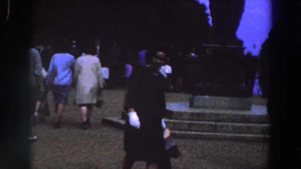 1961 Ireland 8mm frame showing people crossing a plaza beside monument steps in early evening light.