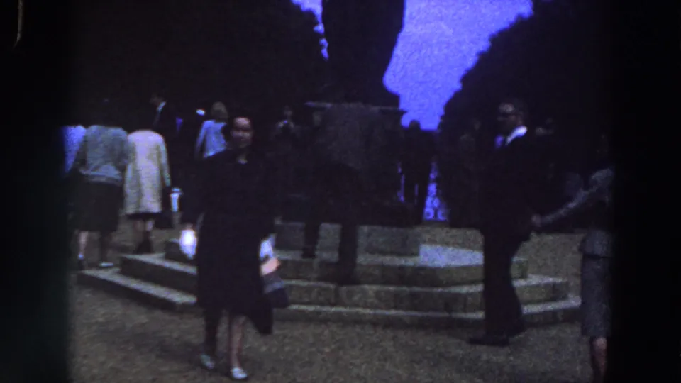 A final 1961 Ireland frame shows the woman centered near stone steps, surrounded by formally dressed visitors in a dim public space.