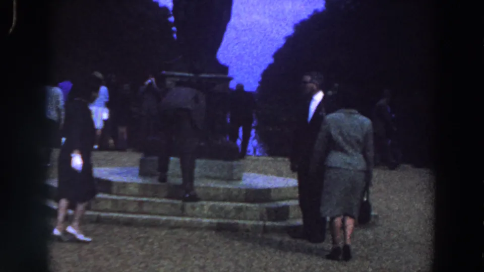 In blue-tinted 8mm footage from Ireland, several adults in mid-century clothing move around the stone steps of a dark monument.