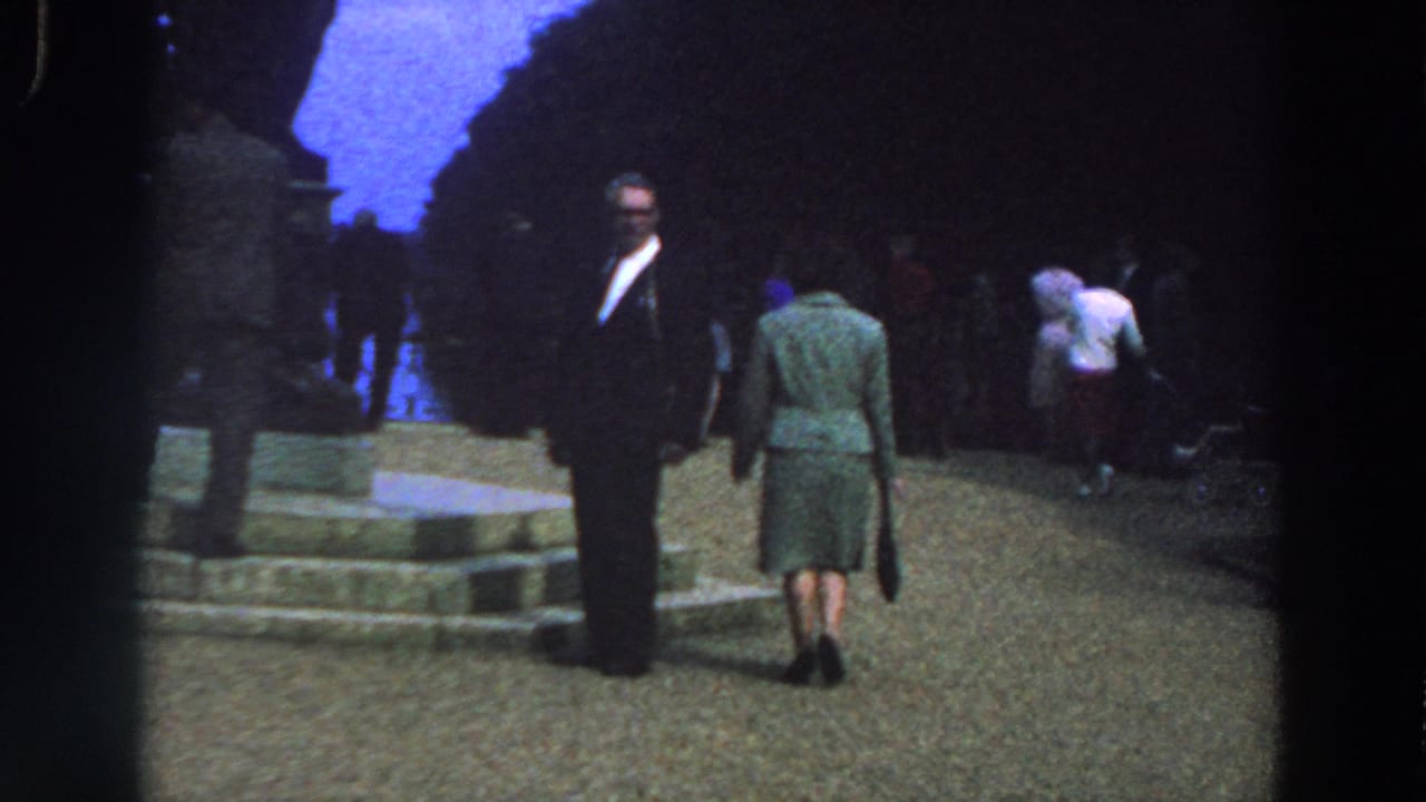 Woman in a green dress walking toward visitors near stone steps.
