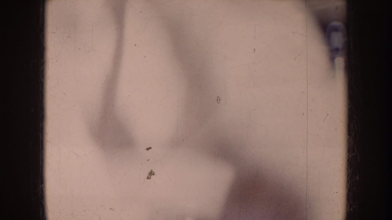 Opening 8mm contact-sheet frame with mostly blank exposed film area, dark vertical gate edges, and faint blurred motion before the football action.