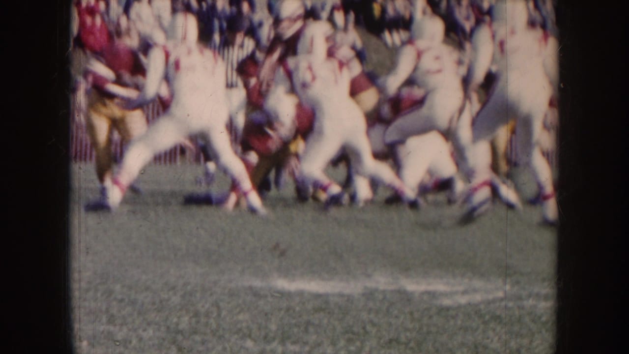 Football players in maroon and white uniforms collide on a grass field.