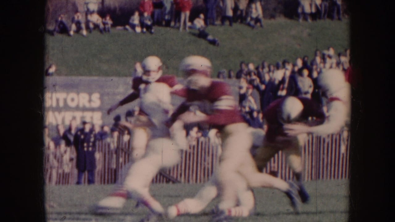 A football player runs while another player reaches to tackle him near spectators.