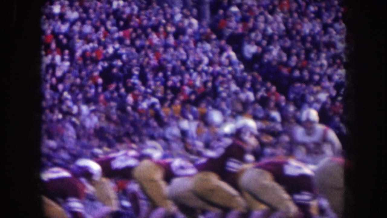 Football players line up near a large hillside crowd.