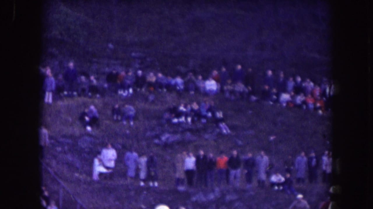 Spectators stand and sit along a grassy hillside.