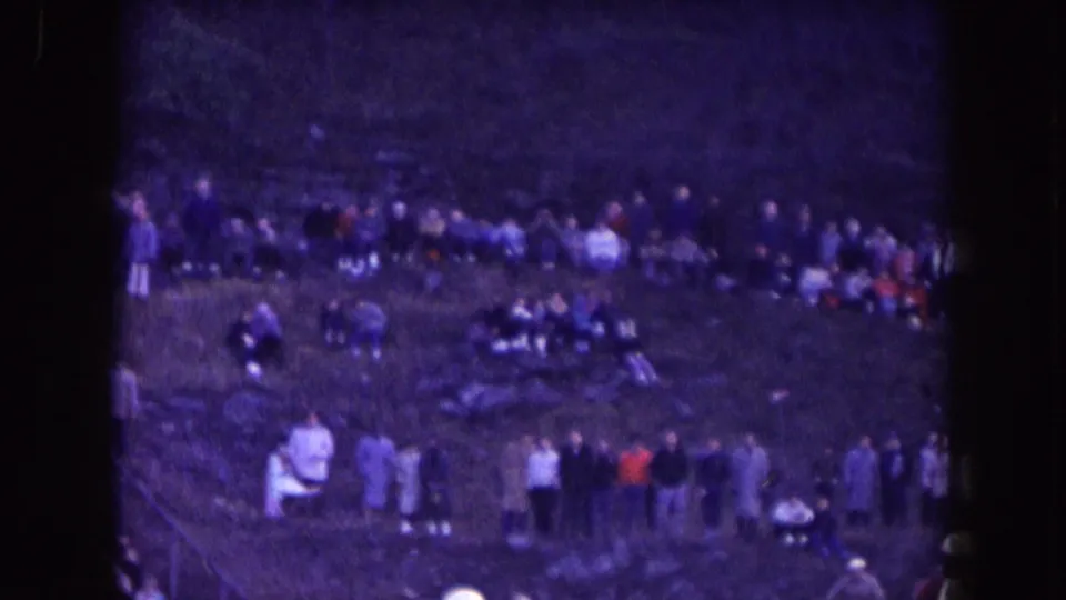 Distant 1957 Nebraska home-movie view of spectators gathered on a grassy slope near a high school football game.