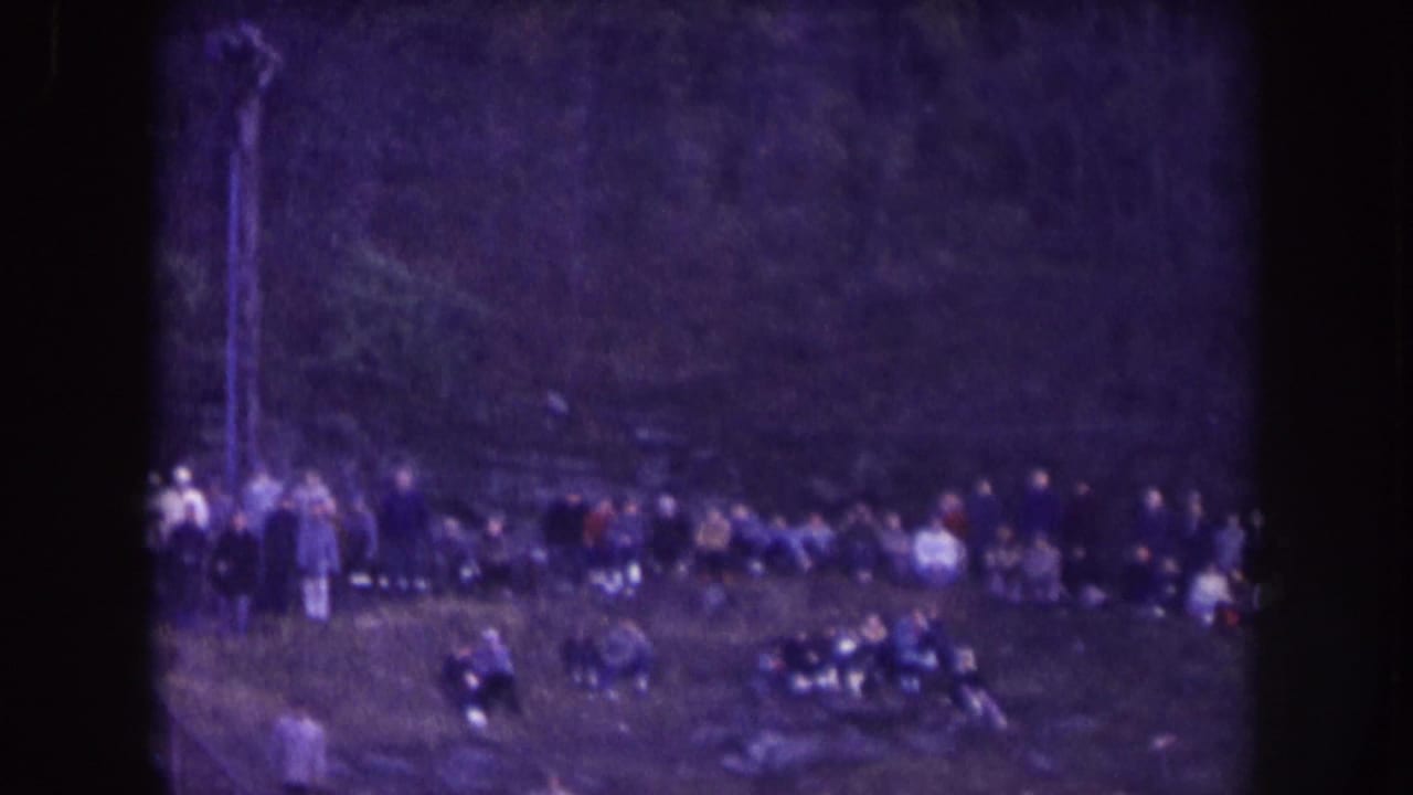 Distant spectators lined along a field or seating area in soft, purple-tinted 8mm footage.