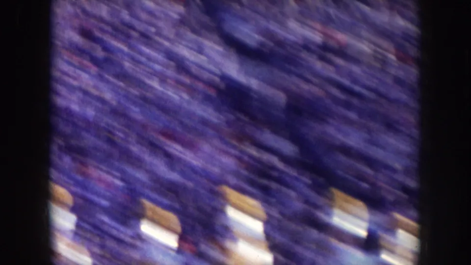 1957 Nebraska 8mm frame showing a blurred, high-angle stadium crowd with a few pale figures near the lower edge.