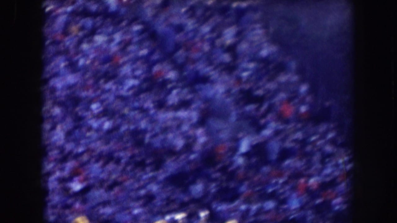 Dense stadium crowd fills the frame, broken by dark shapes and small red and white specks.