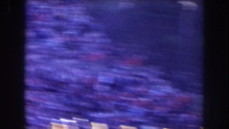 Heavily blurred 8mm frame from the Nebraska stadium crowd, with purple-blue cast and indistinct pale figures below.