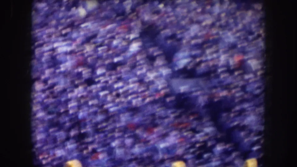 1957 Nebraska home-movie frame of packed stadium seating from above, with indistinct crowd detail and dark film-edge borders.