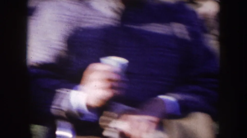 Nebraska 1957 8mm frame of bundled spectators, including a hand holding a white cup in the foreground.