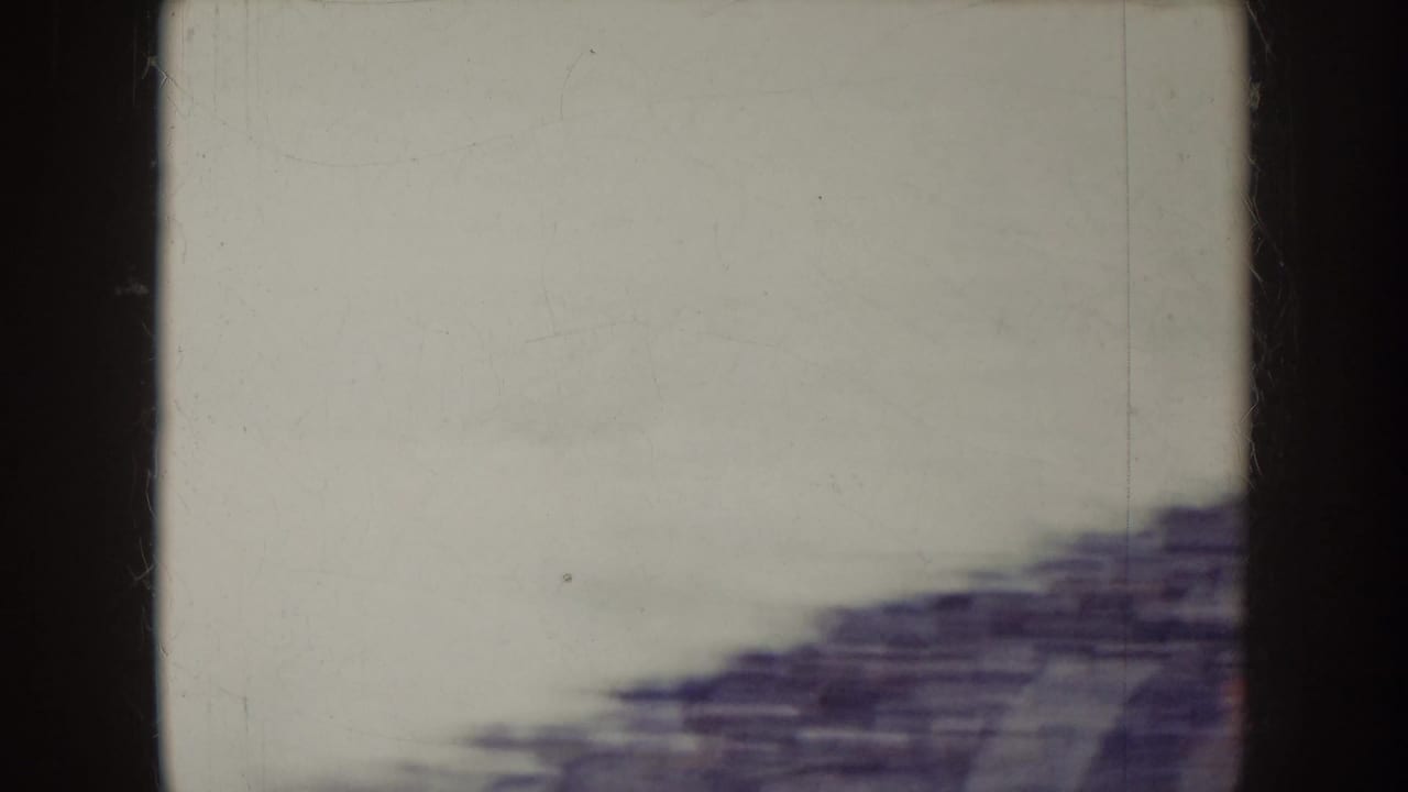 Blurred stadium bleachers beneath a pale sky with dark film borders.