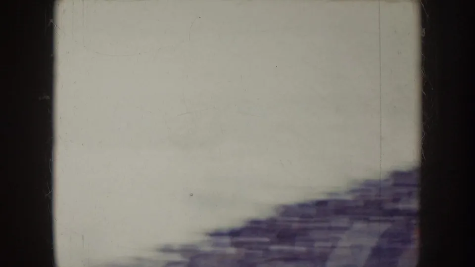 1957 Nebraska 8mm frame showing a pale sky above blurred stadium seating or bleachers, with heavy handheld motion and dark frame edges.