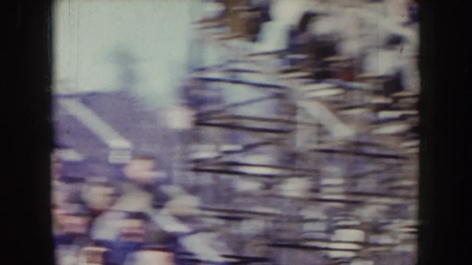1957 Nebraska 8mm frame showing a blurred section of stadium rails or bleachers with indistinct people near the lower edge.