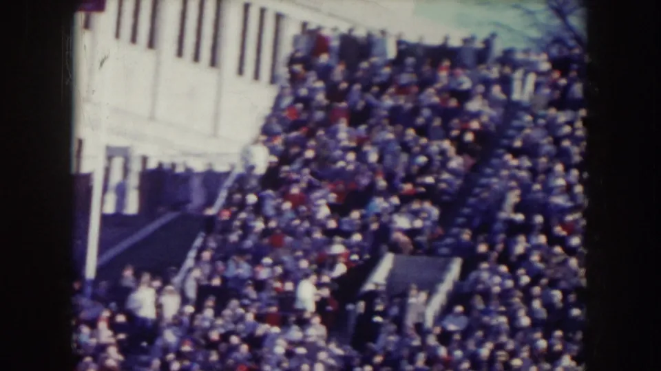 1957 Nebraska 8mm frame showing a packed outdoor crowd near a light-colored building and steps.