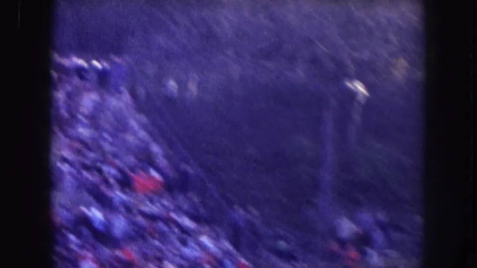 Grainy 1957 Nebraska stadium view showing bleachers along one side and a blurred open area beyond them.