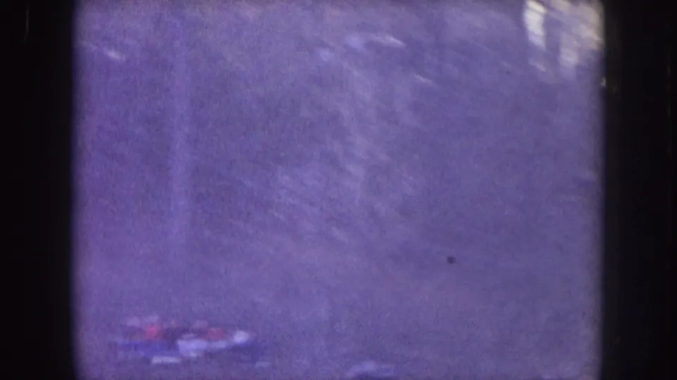 Hazy 8mm frame from the Nebraska stadium clip, with an open area and indistinct crowd detail near the lower edge.