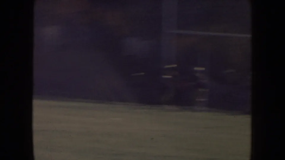 1957 Nebraska home-movie frame with football players faintly jogging across a grassy field, softened by motion blur, grain, and underexposure.