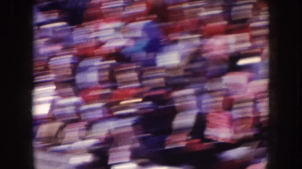 A handheld 8mm view of the Nebraska football crowd, with spectators and sideline shapes blurred by camera motion.