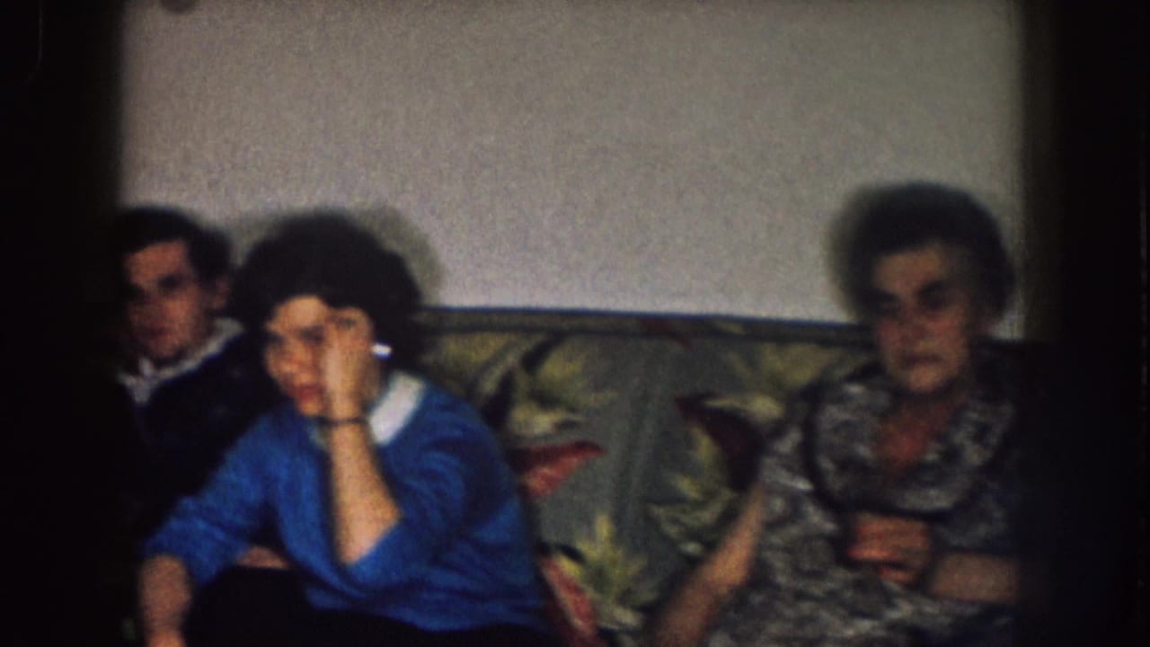 Adults seated on a floral couch, including a woman in blue and an older woman at right.
