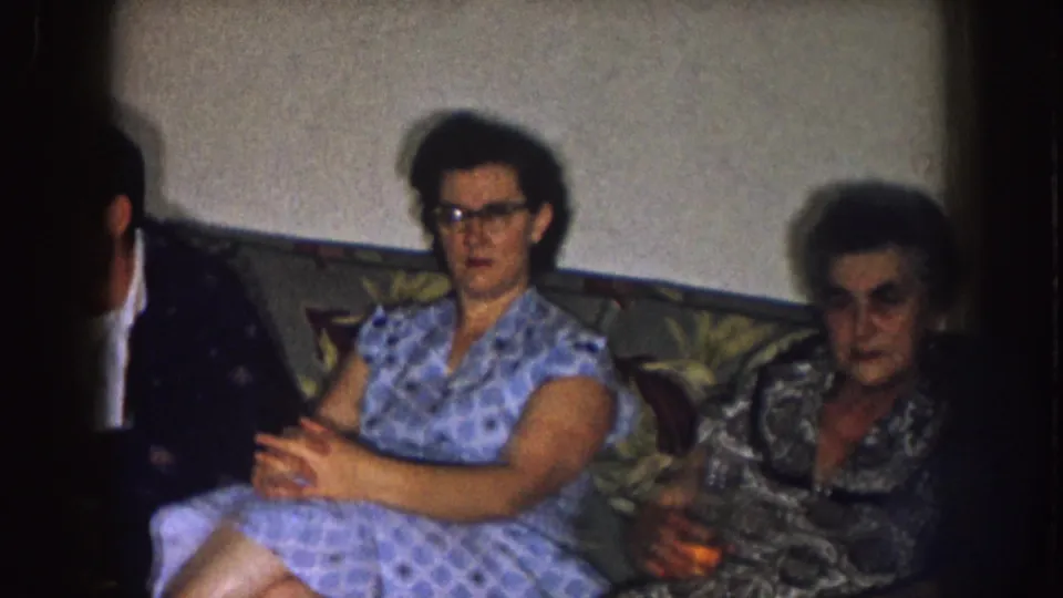 Two women and a partially visible man sit on or near a patterned couch in a 1957 Nebraska home interior.