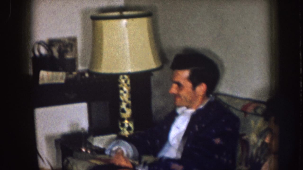 Man seated beside a table lamp in a living room.