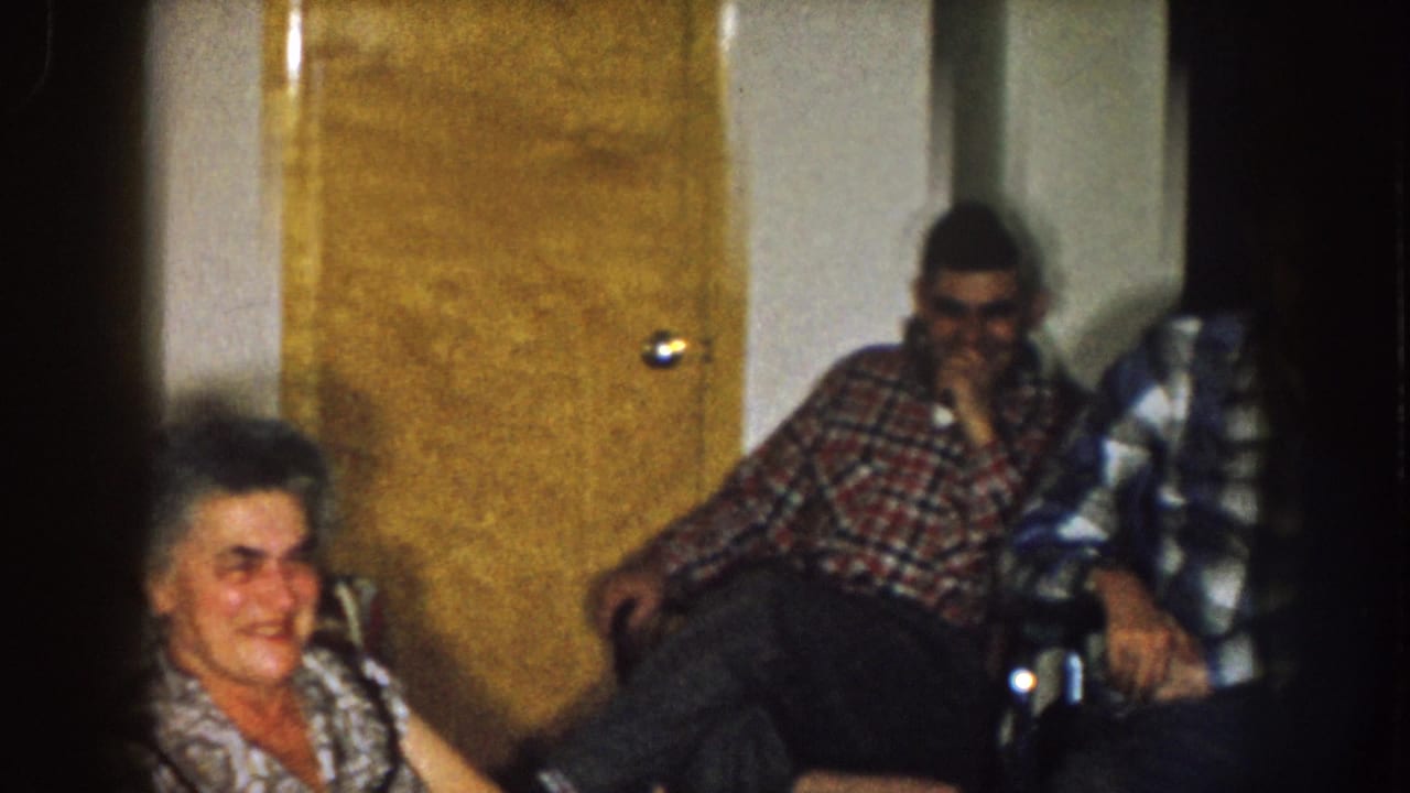 Older woman sits near two adult men in a room with a wooden door.