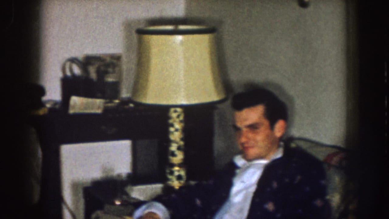 Man seated beside a table lamp in a dim living room.