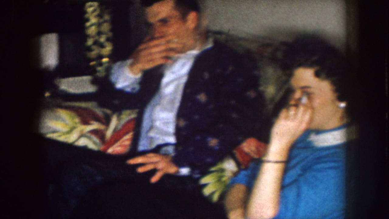 Man and woman seated on a couch, with the man raising a hand near his mouth.