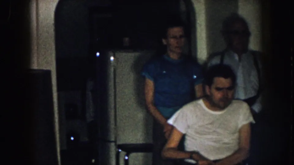 The final frame keeps the man in the wheelchair at the front of the group, with a woman in blue and an older man standing behind him indoors.